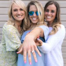 Woman showing off her diamond engagement ring next to two other women.